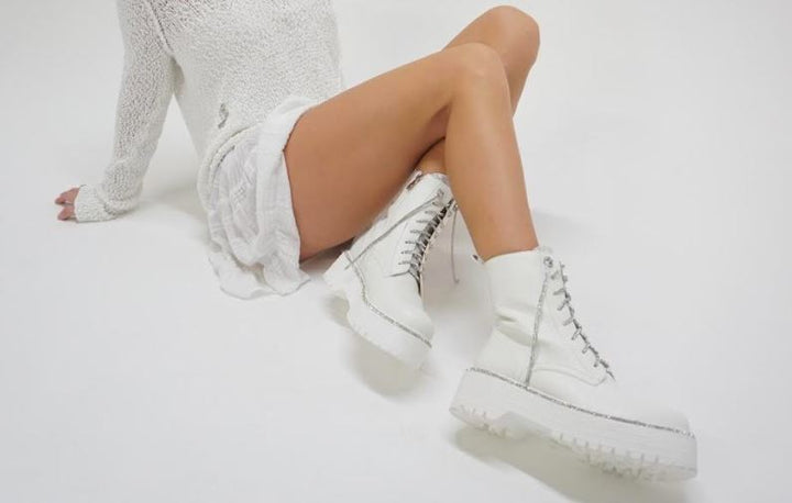 Model wearing white platform combat boots with a white sweater in a white room