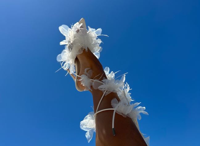 Model wearing white wrap up floral stiletto heels in front of a blue sky