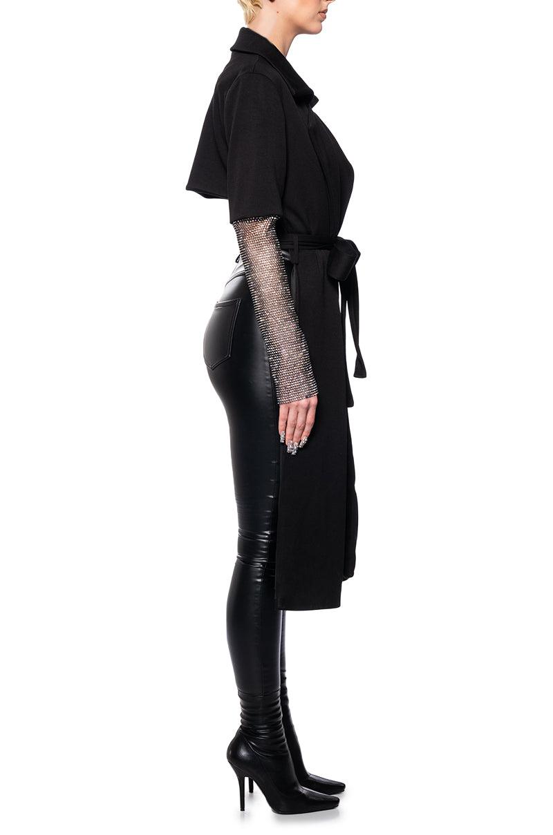 side view of black asymmetrical trench jacket with mesh sleeves and a cropped back side and elongated front that ties in the center