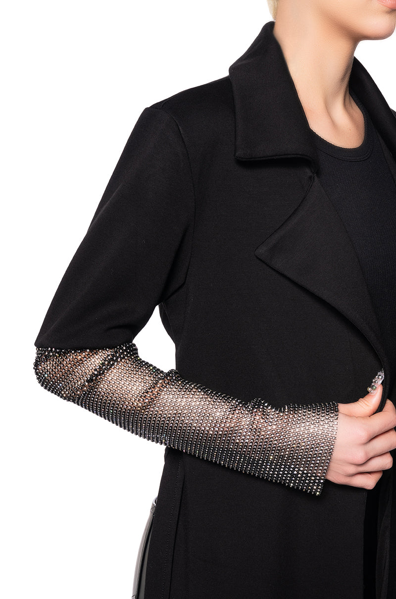 detail shot of black asymmetrical trench jacket with mesh sleeves and a cropped back side and elongated front that ties in the center