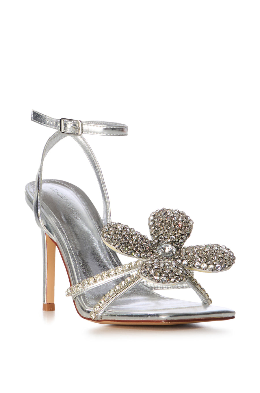 angled view of metallic silver statement open toe heels with a crystal rhinestone embellished foot strap featuring a sparkly flower accent and an adjustable ankle strap closure