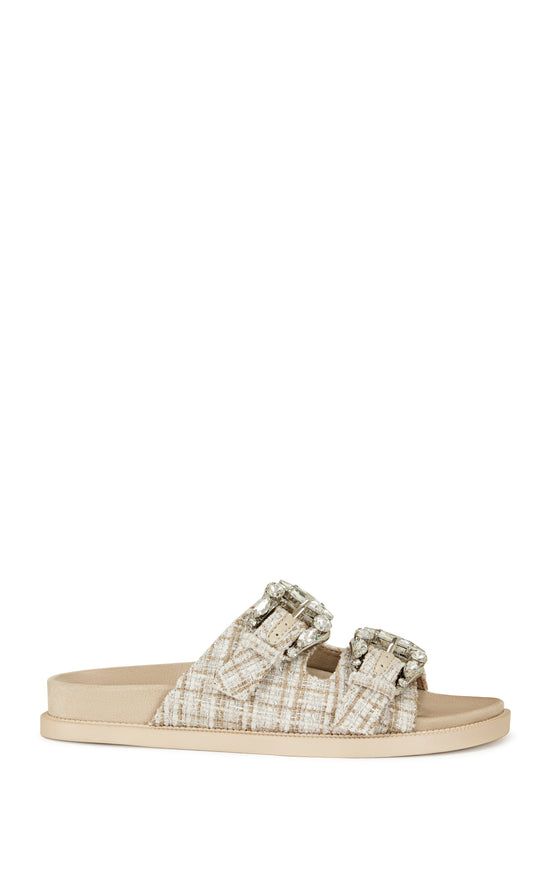 beige slip on flat sandal with a tweed upper with double straps featuring silver rhinestone studded belted accents on each strap