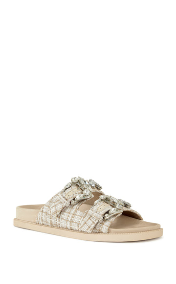 beige slip on flat sandal with a tweed upper with double straps featuring silver rhinestone studded belted accents on each strap