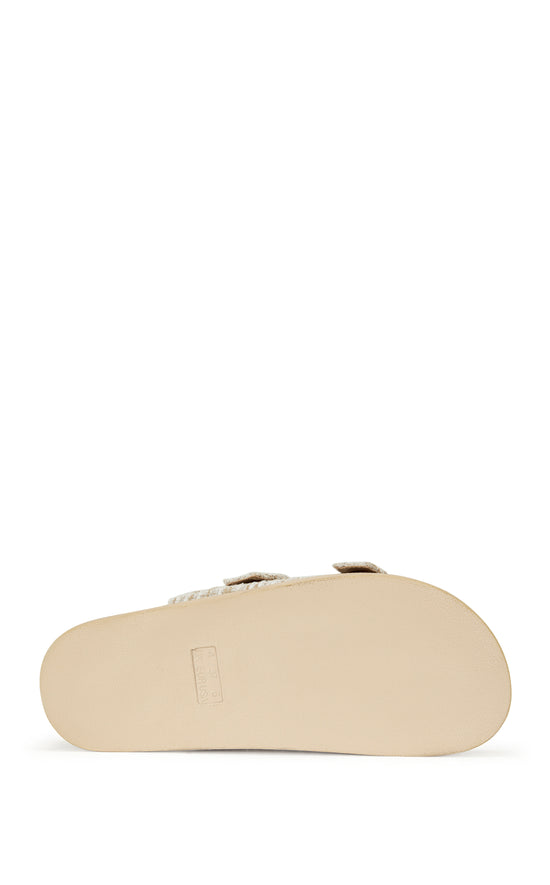 beige slip on flat sandal with a tweed upper with double straps featuring silver rhinestone studded belted accents on each strap