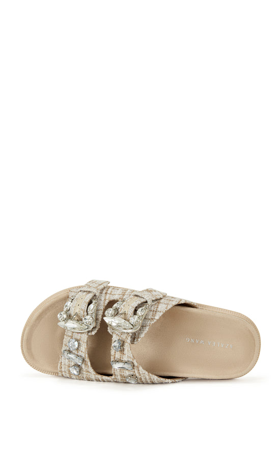 beige slip on flat sandal with a tweed upper with double straps featuring silver rhinestone studded belted accents on each strap