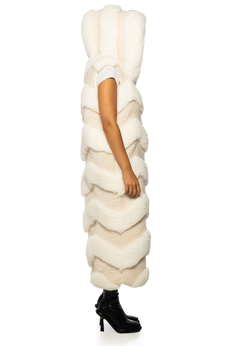 side view of long trench style beige faux fur vest with a chevron fur pattern and a fluffy hood