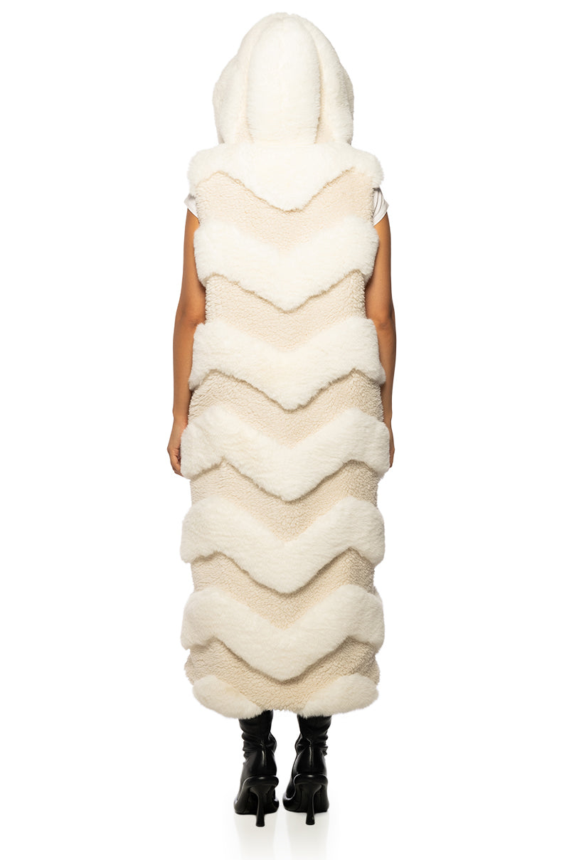 back view of a long trench style beige faux fur vest with a chevron fur pattern and a fluffy hood