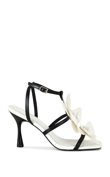 black and white faux leather statement stiletto heels with an open toe design, an adjustable ankle strap, and two oversized white flower accents on the straps