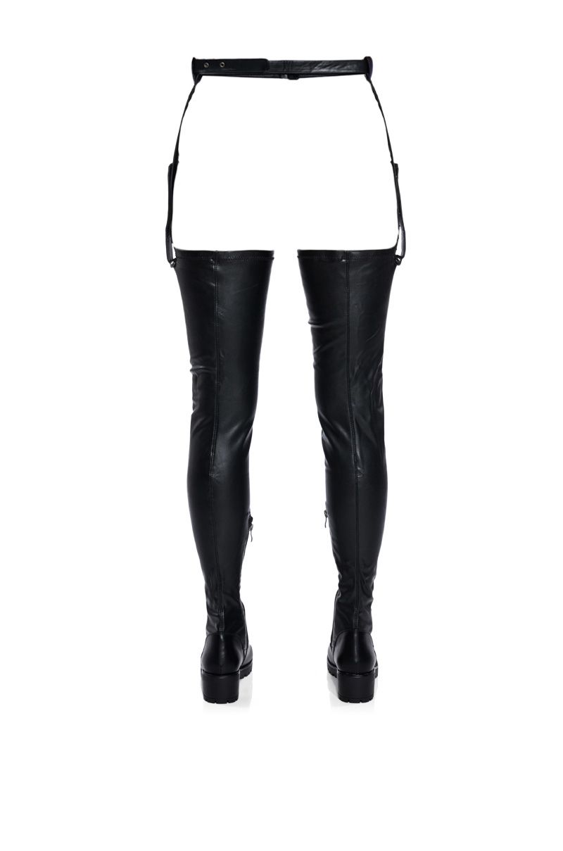 back view of black faux leather 4 way stretch thigh high flat boots with an attached stirrup belt 