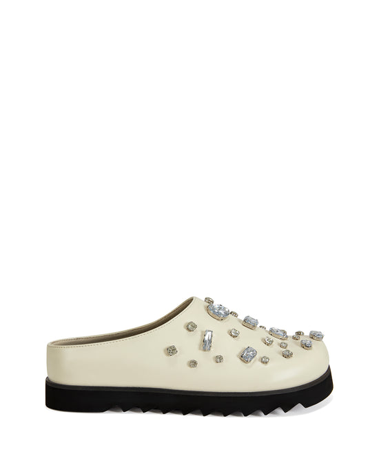 Cream faux leather slip on clog with a black ridged sole and chunky rhinestones embellished on the upper