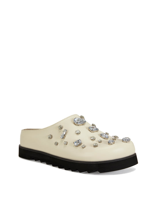 Cream faux leather slip on clog with a black ridged sole and chunky rhinestones embellished on the upper