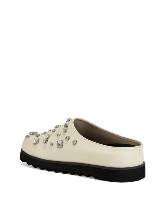 Cream faux leather slip on clog with a black ridged sole and chunky rhinestones embellished on the upper
