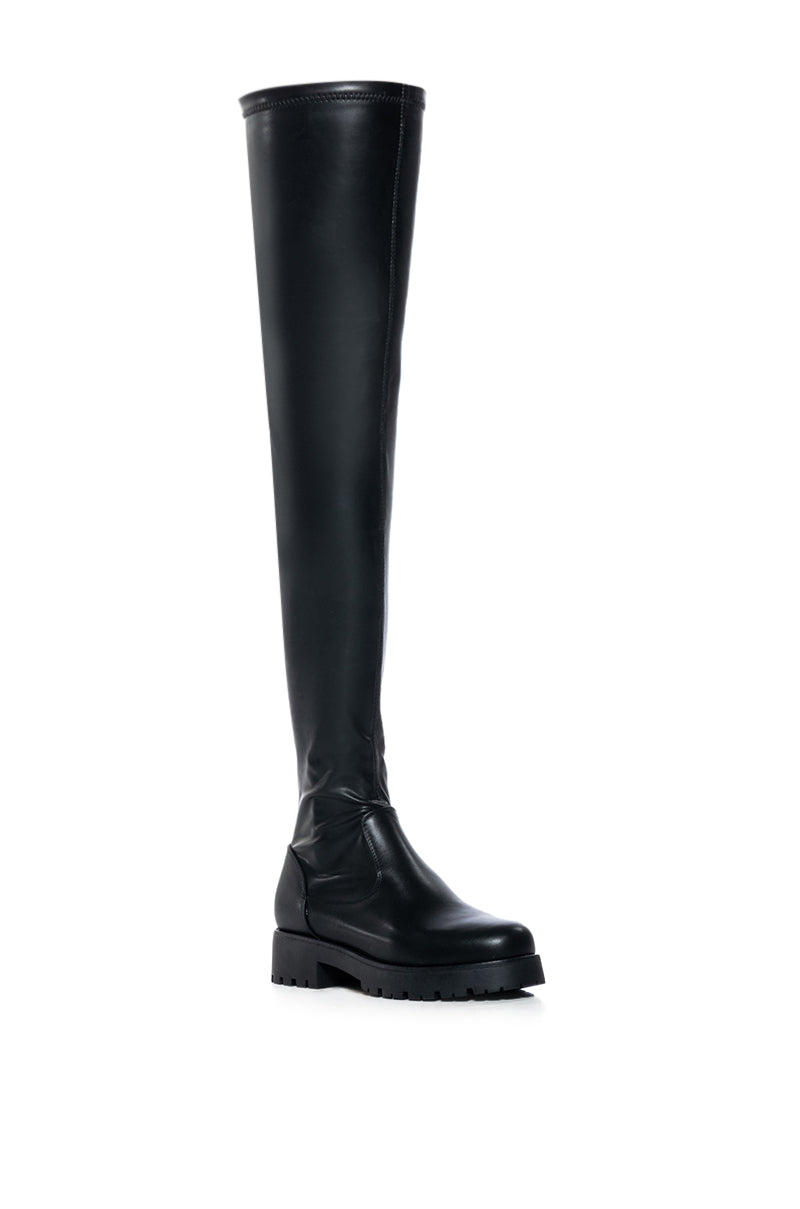 angled view of black faux leather over the knee stretchy flat boot made with 4 way stretch material