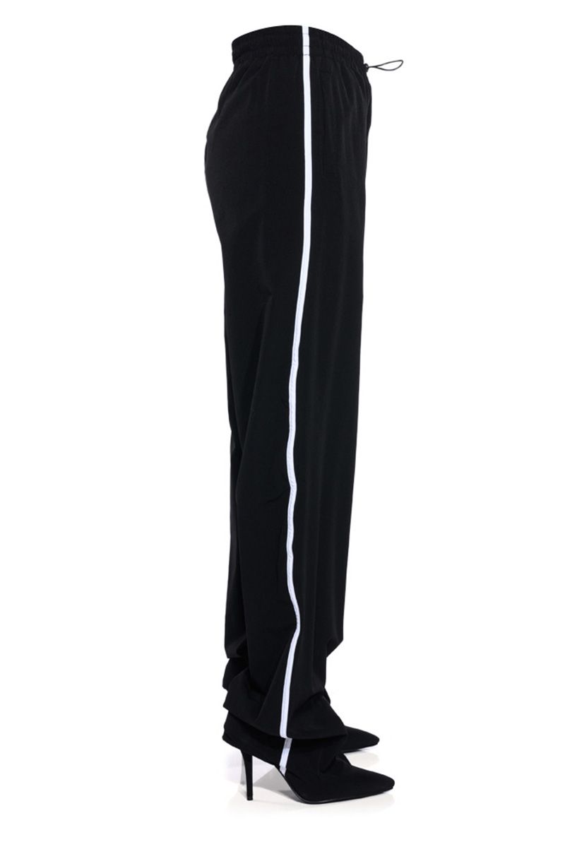 black pointed toe stiletto boots attached to drawstring track pants with white stripe