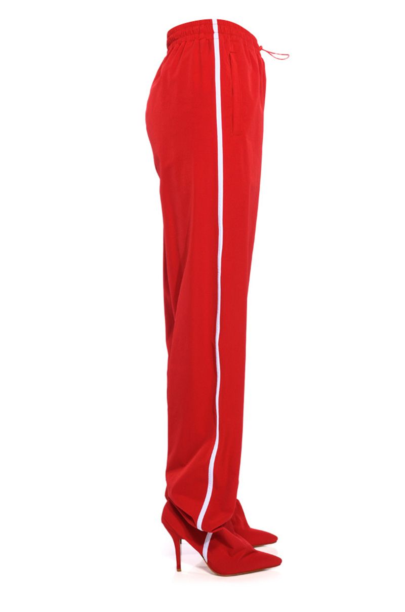bright red pointed toe stiletto boots attached to drawstring track pants with white stripe